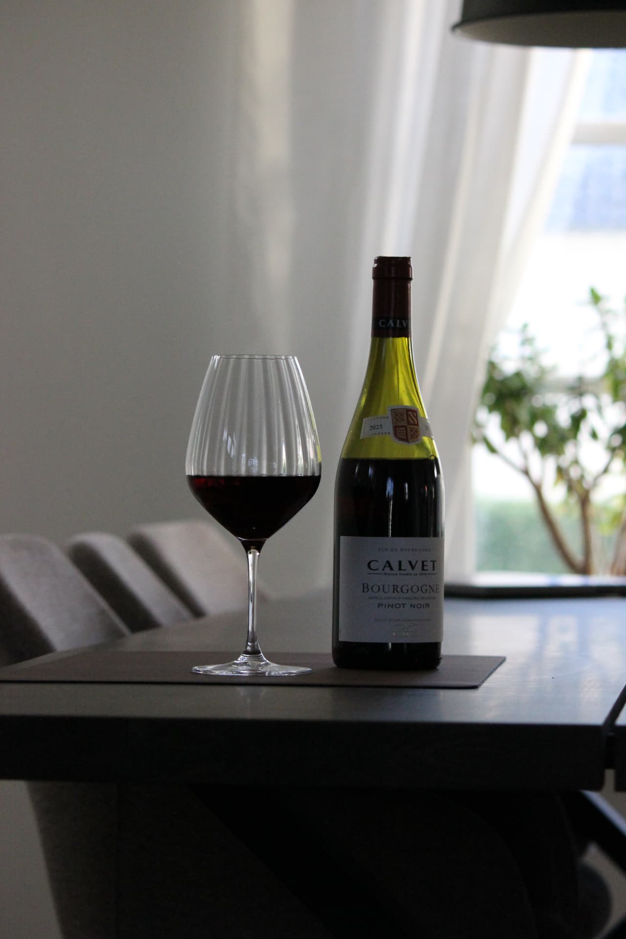 Flaske Bourgogne Pinot Noir og et glas rødvin på et mørkt spisebord